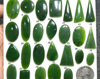 May include: A collection of twenty-five polished green jade cabochons in various shapes including ovals, rectangles, and triangles, arranged on a white board with numbered labels from 1 to 26, alongside a US quarter coin for scale reference.