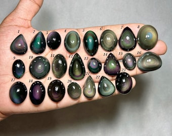May include: A collection of twenty-three polished rainbow obsidian cabochons arranged in rows. Each stone features a smooth, rounded surface with iridescent bands of green, purple, and gold colors. Each individual gemstone is labeled with a number.