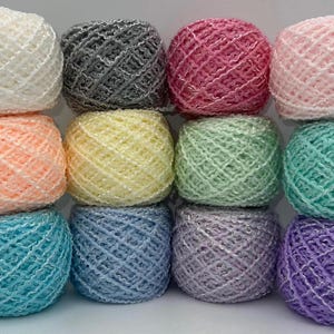 May include: A collection of twelve round balls of yarn arranged in a grid. The yarn features a textured, net-like structure with a subtle shimmer. The colors include white, gray, pink, light pink, peach, yellow, light green, teal, blue, lavender, and purple.