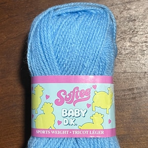May include: A ball of light blue baby yarn with a pink and white label. The label features the word "Softee" in pink script, the words "Baby D.K.", and yellow sheep illustrations. The yarn is sports weight.