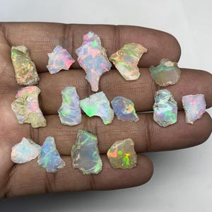 May include: A collection of raw opal gemstones, displaying a variety of shapes and sizes. The opals exhibit iridescent colors, including flashes of blue, green, pink, and yellow. The gemstones are held in a hand, showcasing their natural beauty.