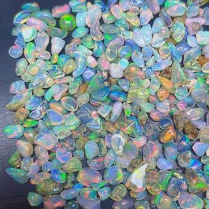 Puede incluir: Una colección de piedras preciosas de ópalo pulidas de varias formas y tamaños. Los ópalos muestran una gama de colores, incluyendo azul, verde, rosa y naranja, con destellos iridiscentes. Las piedras preciosas están dispersas.