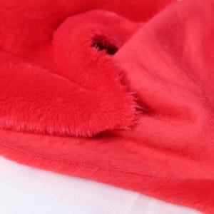 May include: Close-up of vibrant red fabric, showcasing a plush, furry texture on one side and a smooth, woven texture on the other. The fabric is folded, revealing the contrast between the textures. Ideal for crafting or apparel.
