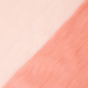 May include: A close-up shot of two sections of faux fur. One section is a soft, creamy white, and the other is a warm, peachy pink. The fur has a long, fluffy texture, creating a diagonal color block effect.