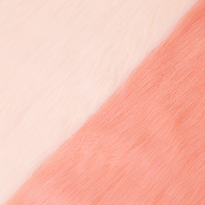 May include: A close-up shot of two sections of faux fur. One section is a soft, creamy white, and the other is a warm, peachy pink. The fur has a long, fluffy texture, creating a diagonal color block effect.