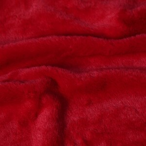 May include: Close-up of a vibrant red faux fur fabric. The plush material has a soft, textured appearance with visible fibers and subtle variations in color. The fabric's surface is slightly wavy, creating shadows and highlights.
