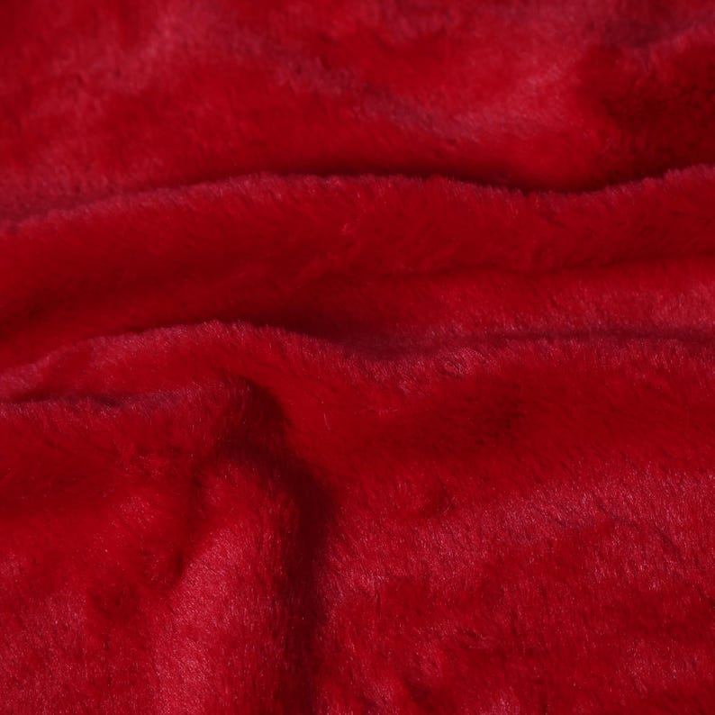 May include: Close-up of a vibrant red faux fur fabric. The plush material has a soft, textured appearance with visible fibers and subtle variations in color. The fabric's surface is slightly wavy, creating shadows and highlights.