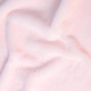 May include: Close-up of a soft, light pink faux fur fabric. The plush material has a dense pile and a subtle sheen, with gentle folds and shadows creating depth. The overall texture appears smooth and inviting.