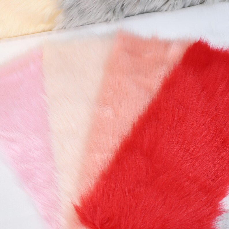 May include: A close-up view of several faux fur fabric samples in various shades of pink and red. The colors transition from light pink to a vibrant red, with a soft, fluffy texture.