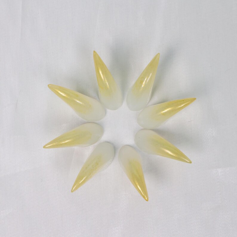 May include: Eight long, pointed, artificial fingernails arranged in a circular pattern. The nails transition from a white base to a yellow-gold tip, creating a gradient effect. The nails are set against a white background.