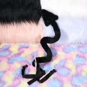 Flat lay of the tail next to common items for scale, including a coiled belt and a paperback book. The tail spans a generous length suited for photos where the curve frames the wearer. The belt loop sits above the base for balance so the tail hangs naturally when relaxed. Lighting is soft to preserve detail in darker fabric. This angle communicates thickness, flexibility, and how the tail can be packed in a suitcase without creasing, then reshaped easily on arrival at a hotel.