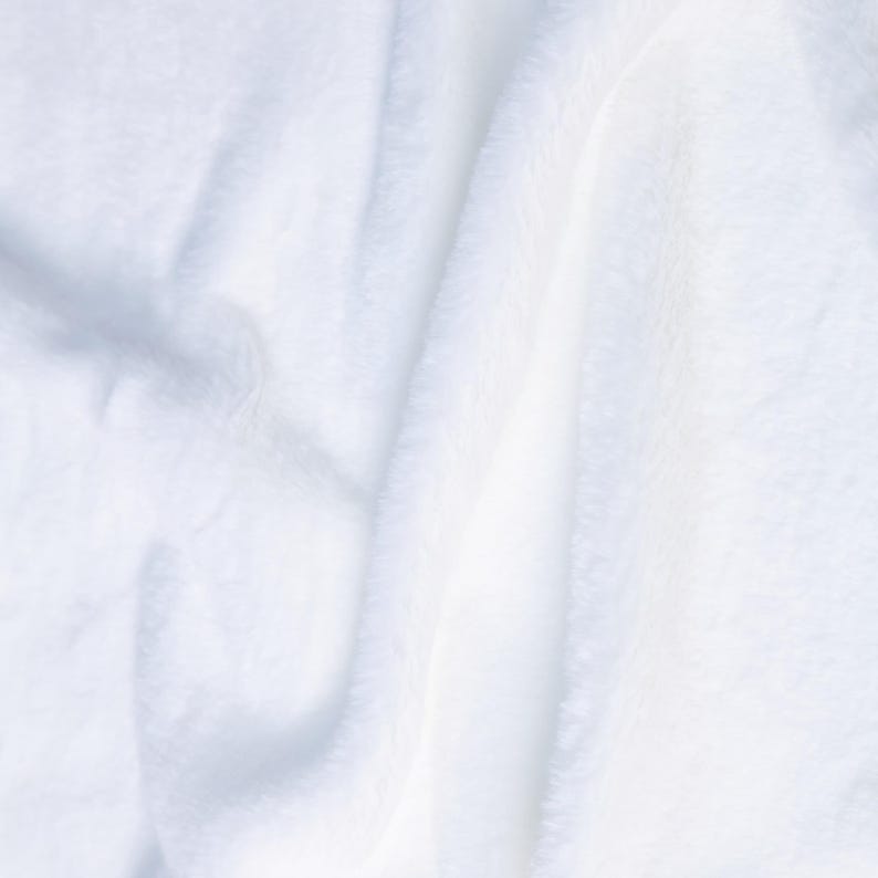 May include: Close-up of a soft, white, fluffy blanket. The fabric has a plush texture with visible folds and shadows, creating a sense of depth. The overall appearance is clean and inviting, suggesting comfort and warmth.