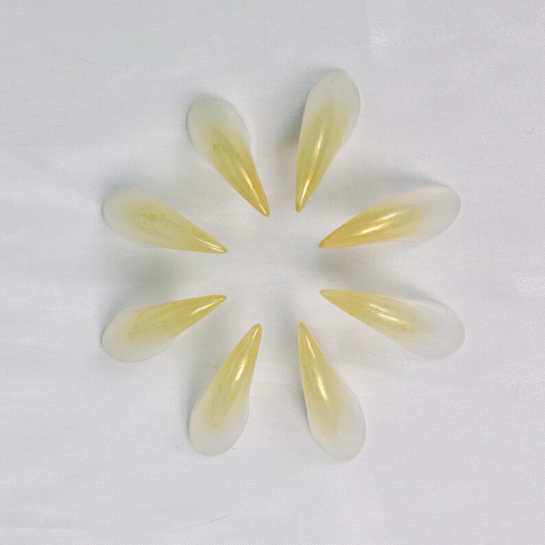 May include: Arrangement of ten translucent, teardrop-shaped objects with a gradient of yellow to white. The objects are arranged in a circular pattern, resembling petals or a stylized sun, against a white background.
