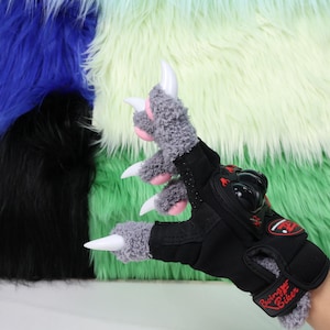 May include: A black and grey motorcycle glove with a claw design. The glove has white claws, grey fur, and pink accents. The words "Racing Biker" are printed on the wrist strap. The background is a colourful, furry texture.