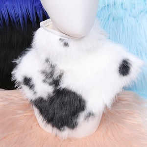 May include: A white faux fur collar with black spots, displayed on a mannequin head. The collar has a fluffy texture and a cow-like pattern. The background features blue, black, and pink faux fur.
