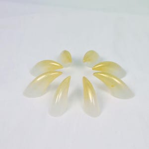 May include: A collection of eight artificial fingernails, arranged in a circular pattern. The nails are a gradient of white to yellow, with a glossy finish. The tips are a vibrant yellow, while the base is a translucent white.