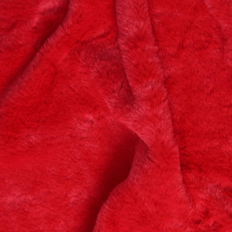 May include: Close-up of a vibrant red faux fur fabric. The plush material has a soft, textured appearance with visible fibers and subtle variations in color, creating a luxurious look. The fabric is folded, showing depth and dimension.