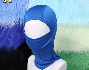 Puede incluir: Una balaclava azul vibrante, diseñada para cubrir la cabeza y el cuello, con una abertura para los ojos y la boca. La balaclava se muestra en una cabeza de maniquí blanca. El fondo presenta piel sintética colorida en tonos azules y verdes.