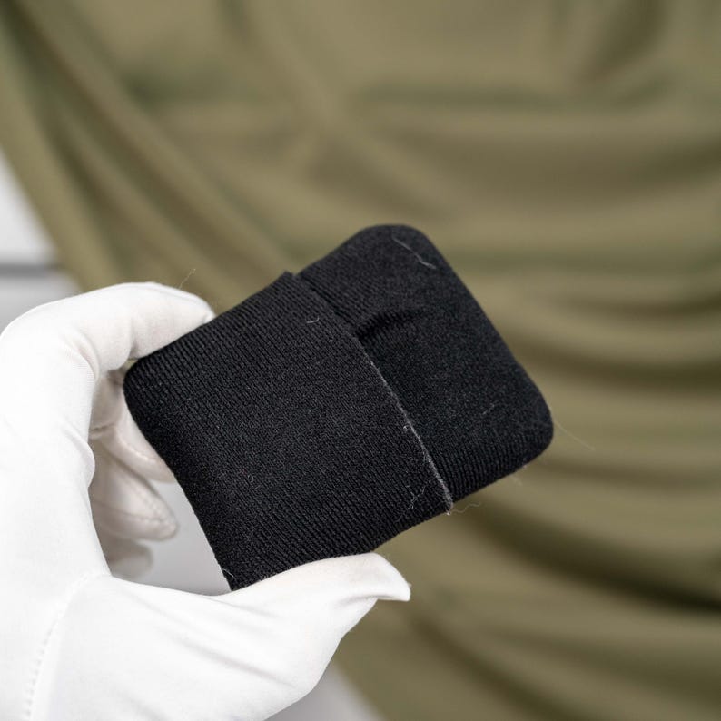 May include: A rectangular black fabric wristband or sweatband featuring a soft, knit texture. The accessory is constructed from a solid black material with a visible seam running vertically across the center, providing a simple and functional design.