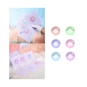 May include: White square cards with pastel-colored bunny stickers. The stickers are in various colors, including pink, purple, green, and blue. The cards are on a fluffy, multi-colored surface.