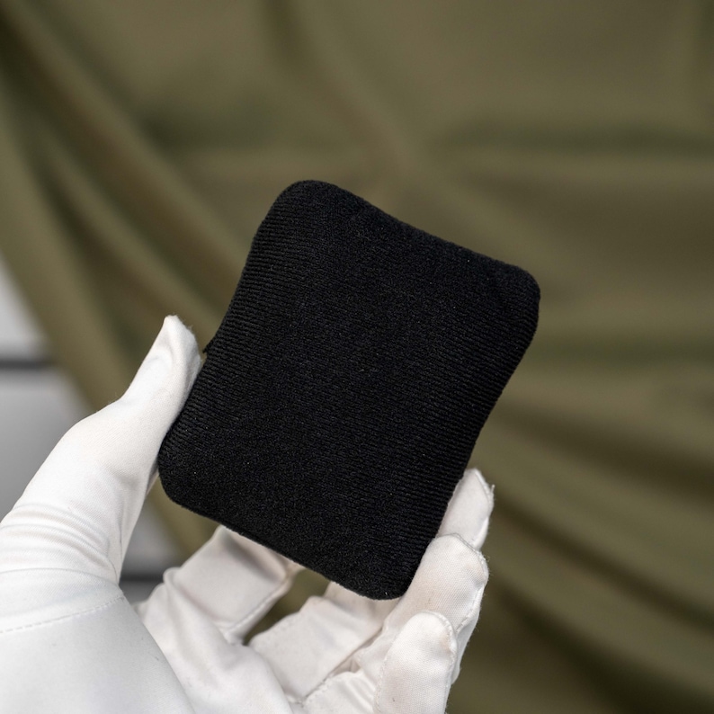 May include: A small, rectangular, solid black fabric pouch with a fine-knit texture. The item features rounded corners and a consistent, matte black finish across its entire visible surface, presenting a simple, uniform, and compact design.