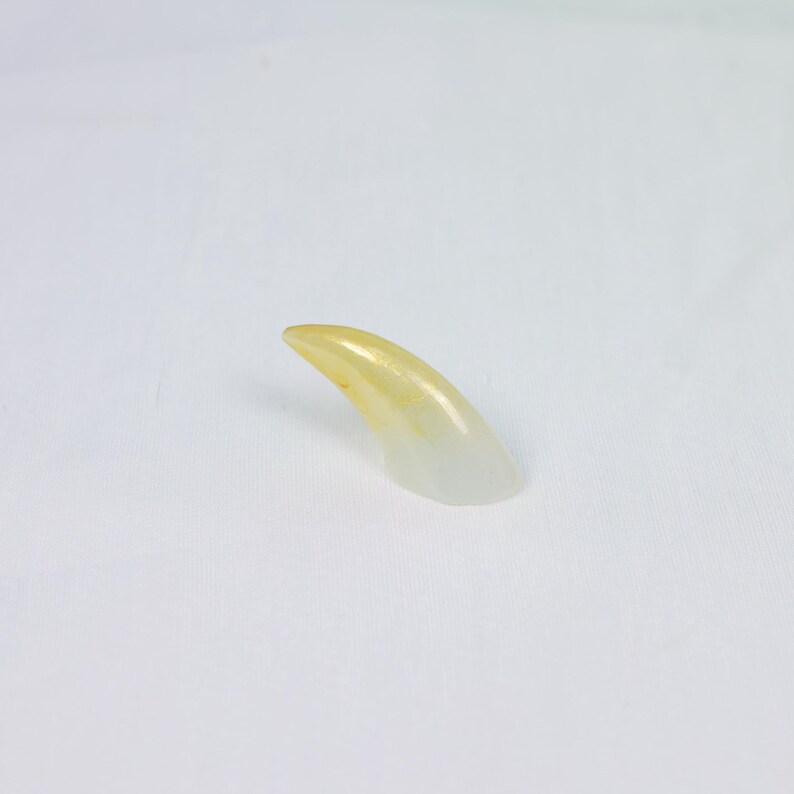 May include: A single, translucent, claw-shaped object with a gradient of yellow to clear. The claw is curved and appears to be made of a smooth, polished material. The background is plain white.