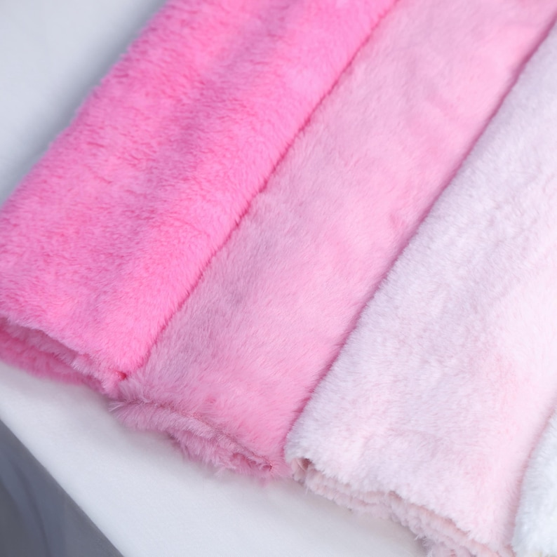 May include: Close-up of three plush, fluffy fabrics in shades of pink, from a vibrant hot pink to a soft, pale pink. The textures appear soft and luxurious, suggesting a cozy material.