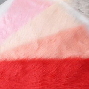May include: A close-up of a soft, faux fur fabric in a gradient of colors. The colors transition from light pink to white, then to peach, and finally to a vibrant red. The texture is fluffy and dense.