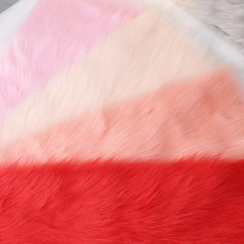 May include: A close-up of a soft, faux fur fabric in a gradient of colors. The colors transition from light pink to white, then to peach, and finally to a vibrant red. The texture is fluffy and dense.