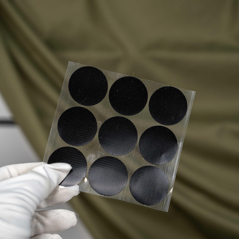 May include: A square transparent sheet containing nine circular black adhesive patches arranged in a three-by-three grid. Each patch features a fine, textured, cross-hatched surface pattern, designed for repair or reinforcement applications.