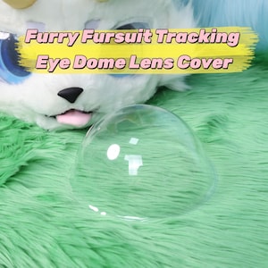 May include: A transparent, domed lens cover for a furry fursuit, set on a green, fluffy surface. The text "Furry Fursuit Tracking Eye Dome Lens Cover" is displayed in a yellow banner. The background features a white and blue furry head.