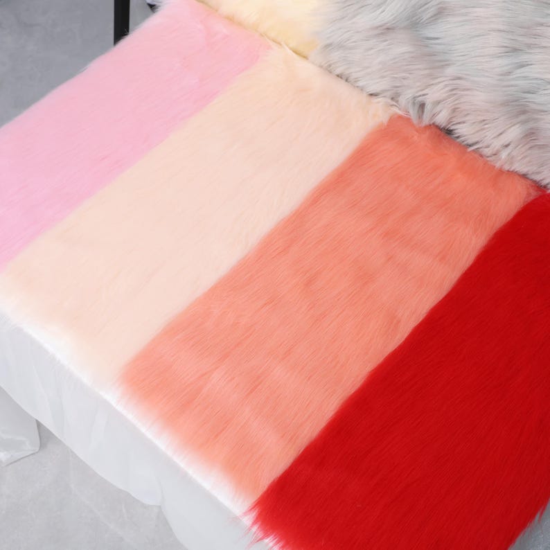 May include: A colorful faux fur fabric with stripes of pink, peach, coral, and red. The soft, fluffy material is arranged in a diagonal pattern, creating a visually appealing texture. The fabric is likely used for crafts or home decor.