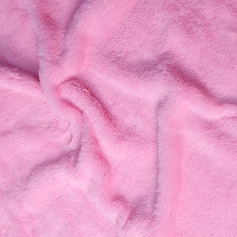 May include: Close-up of a soft, pink faux fur fabric. The plush material has a wavy texture with visible fibers, creating a luxurious and inviting appearance. The color is a vibrant, solid pink, suitable for various craft and design projects.