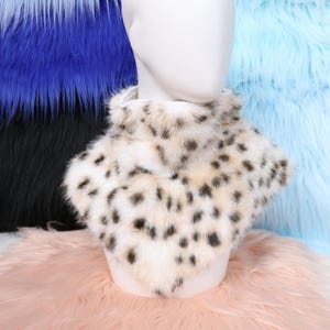 May include: A faux fur collar in cream with black spots, displayed on a white mannequin head. The collar is surrounded by colorful faux fur in blue, black, and pink.