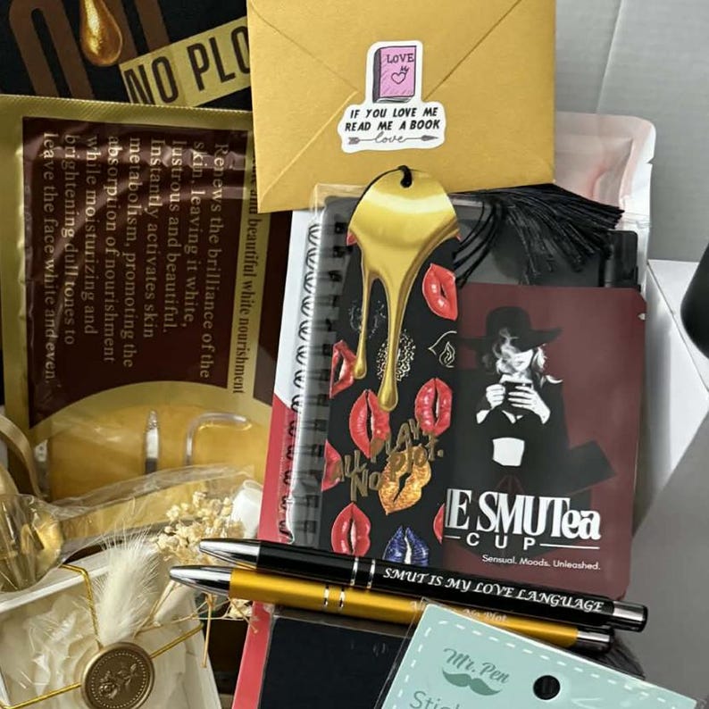 May include: A gift box with various items, including a gold-colored bookmark, a notebook with red lips, and pens. The box also contains a small envelope with a sticker that reads "If you love me read me a book". The notebook has the text "ESMUTea - Sensual, Moods. Unleashed."