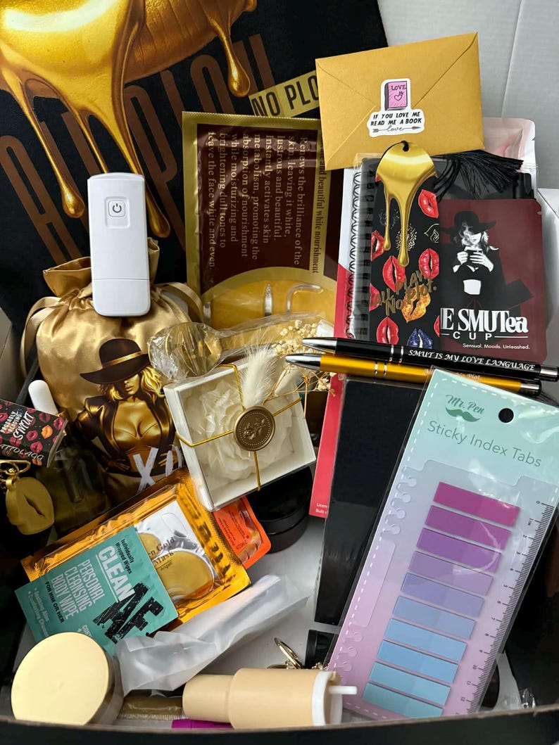 May include: An open box filled with various items, including a white device, a gold-colored statue, a notebook with red lips, pens, sticky index tabs, and skincare products. The box has a black background with gold dripping liquid.