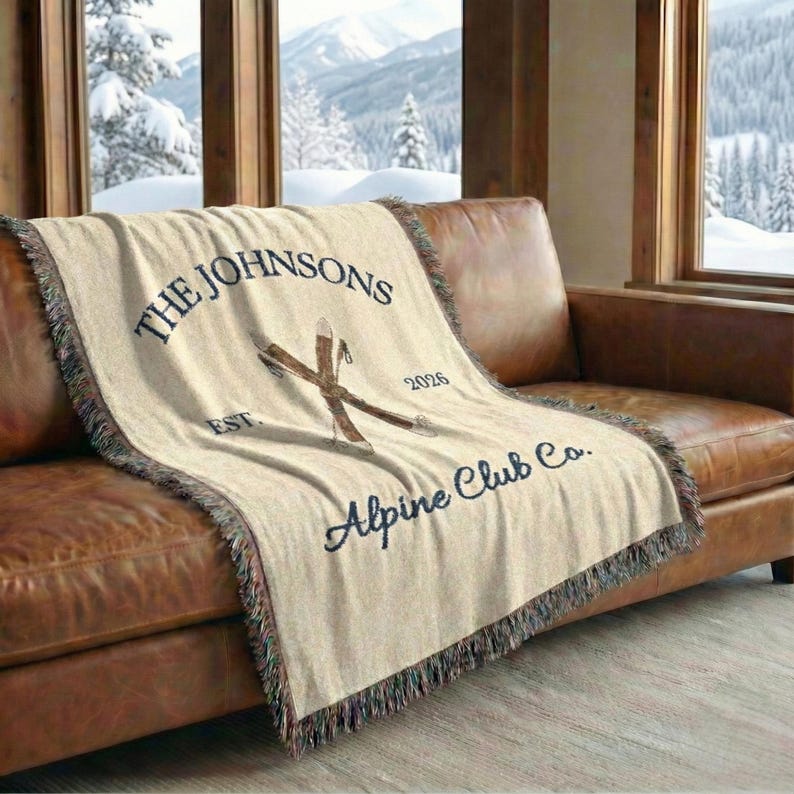 Alpine blanket draped over couch in cozy ski chalet livingroom, cream woven throw with fringes, custom family name, cabin name, location