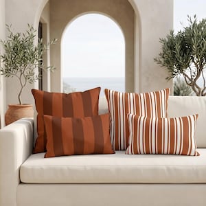 May include: A collection of four throw pillows arranged on a sofa. Two pillows feature wide vertical stripes in shades of terracotta and dark brown, while the other two pillows display thin vertical stripes in terracotta and white.