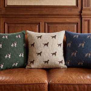 May include: Three square throw pillows featuring a repeating pattern of brown and white dog silhouettes. The left pillow is dark green, the center pillow is beige, and the right pillow is navy blue. Each pillow has a textured fabric finish.