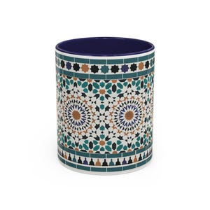 May include: A ceramic coffee mug with a detailed geometric pattern in teal, brown, and white. The interior of the mug is a deep blue. The design features star and mosaic elements, creating a decorative and artistic look.