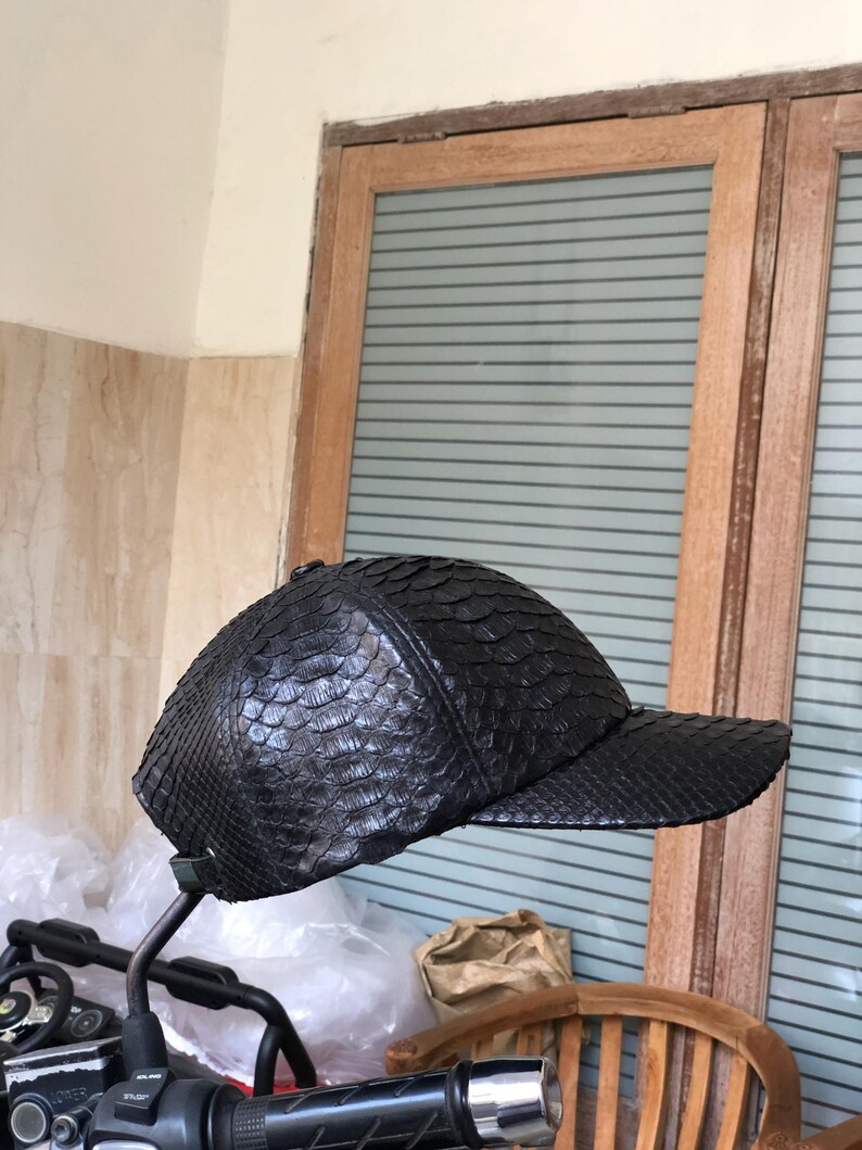 May include: A black baseball cap featuring a textured, scale-like pattern across the entire exterior surface. The cap has a rounded crown and a stiff, horizontal brim extending from the front, showcasing a uniform dark finish throughout.