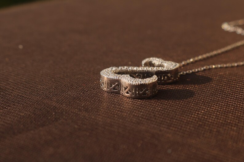 May include: A silver pendant necklace with a cursive letter "S" design. The pendant is encrusted with small, sparkling stones. The necklace chain is delicate and silver. The pendant is approximately 1 inch in length.