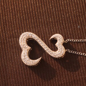 May include: A gold-toned pendant necklace featuring an infinity symbol design. The pendant is encrusted with small, sparkling crystals. The necklace has a delicate chain.