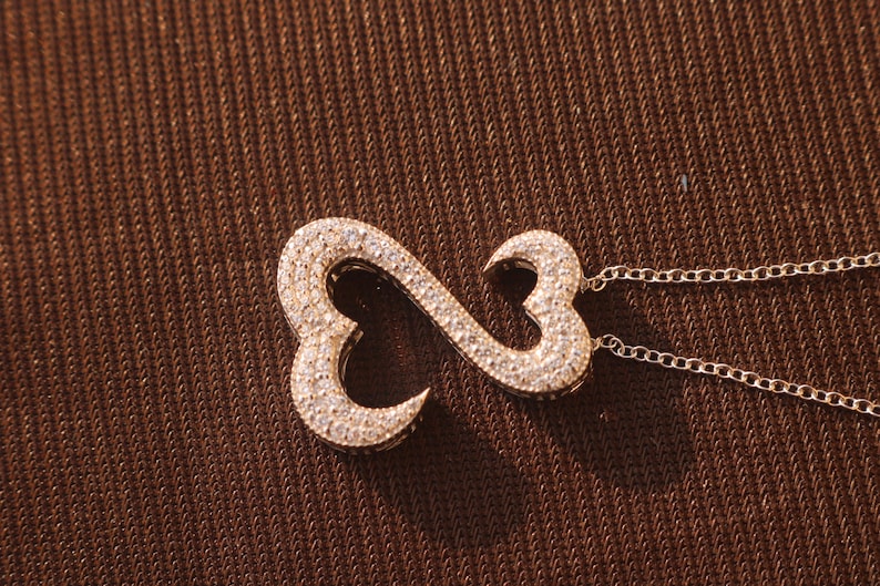 May include: A gold-toned pendant necklace featuring an infinity symbol design. The pendant is encrusted with small, sparkling crystals. The necklace has a delicate chain.