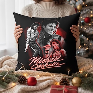 Puede incluir: Cojín cuadrado negro con un collage de imágenes de Michael Jackson en rojo y blanco. El cojín tiene un fondo negro con el nombre "Michael Jackson" en cursiva roja.