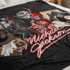 May include: Black blanket with a graphic of Michael Jackson and the text "Michael Jackson". A brown fedora, a white glove, and vinyl records are arranged on the blanket. A photograph of Michael Jackson is also visible.
