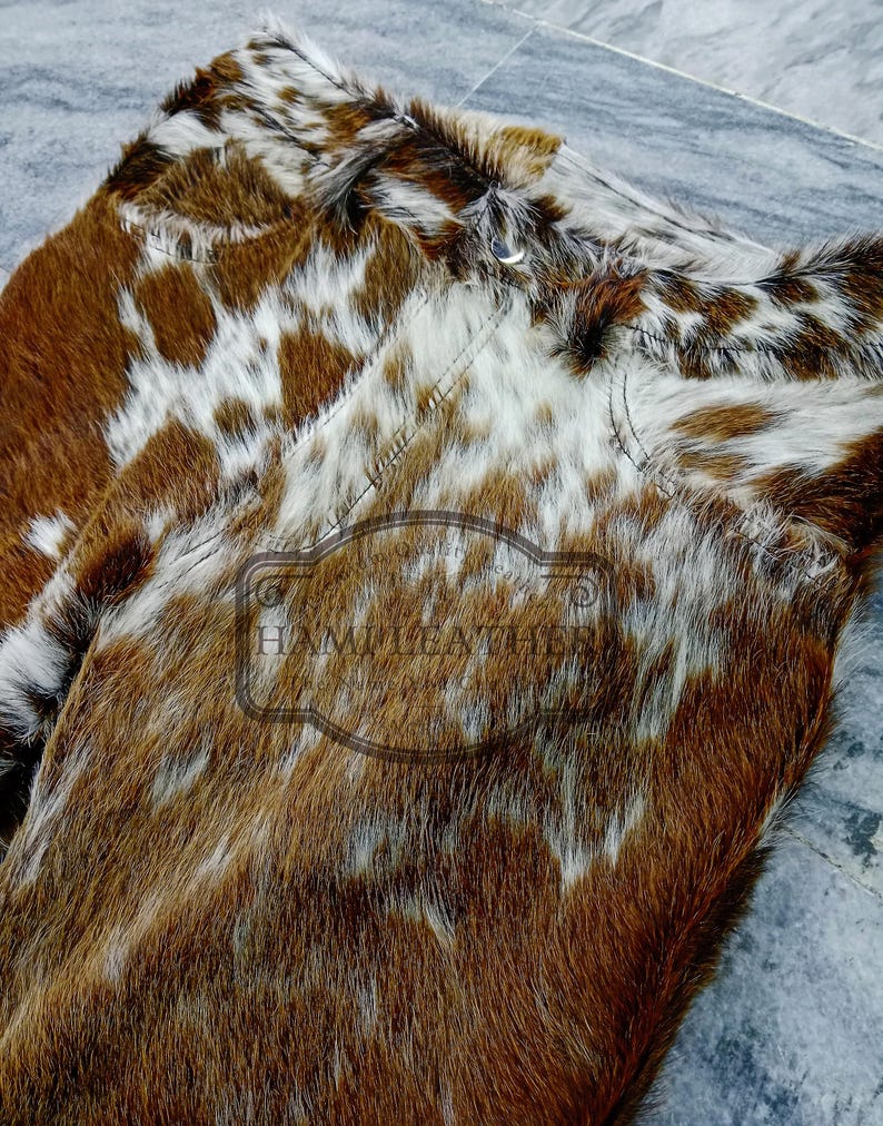K&ouml;nnte beinhalten: Nahaufnahme von zwei St&uuml;cken Rindsleder. Das Leder hat ein nat&uuml;rliches Muster aus braunen und wei&szlig;en Flecken. Die Textur des Fells ist sichtbar, und die N&auml;hte sind entlang der Kanten sichtbar. Der Text "HAMI LEATHER" ist sichtbar.
