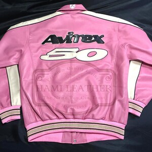 Op de afbeelding: Roze leren jas met witte en zwarte accenten. De achterkant toont de merknaam "Avirex" boven het nummer "50". De jas heeft een geribbelde kraag en manchetten. De tekst "Hami Leather" is ook zichtbaar.