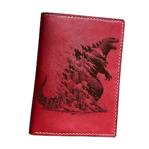 May include: A red leather passport holder with a detailed brown illustration of Godzilla destroying a city. The design features the iconic monster amidst smoke and skyscrapers, with a stitched border.