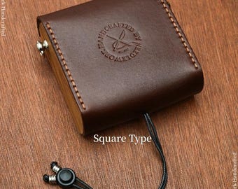 Könnte beinhalten: Ein braunes quadratisches Lederetui mit Holzbasis, mit einem genähten Design und einem schwarzen, verstellbaren Umhängegurt. Das Etui hat ein rundes Logo mit der Aufschrift "Handcrafted by Needlework". Der Text "Square Type" ist ebenfalls sichtbar.